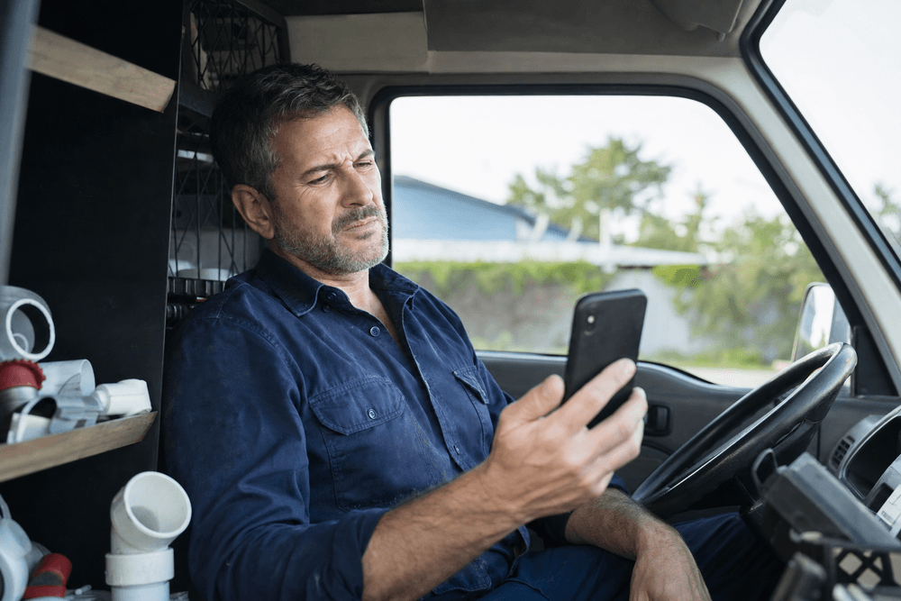A plumber squinting at his slow-loading website on a phone in his work van.