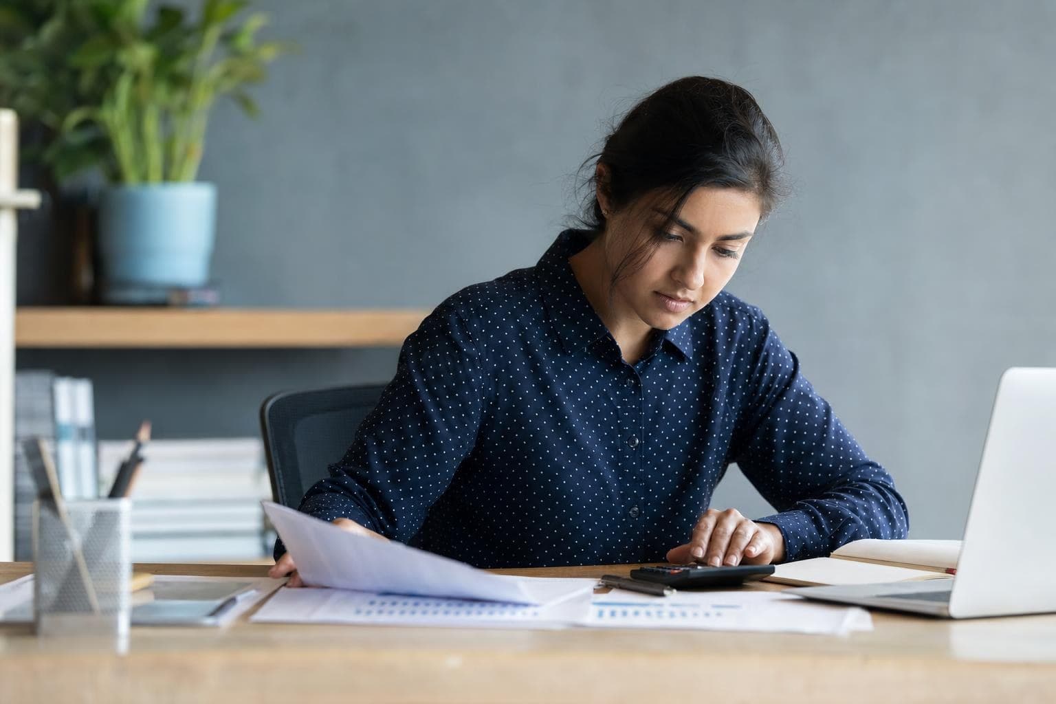 An owner reviewing numbers on a spreadsheet and a calculator at her desk.