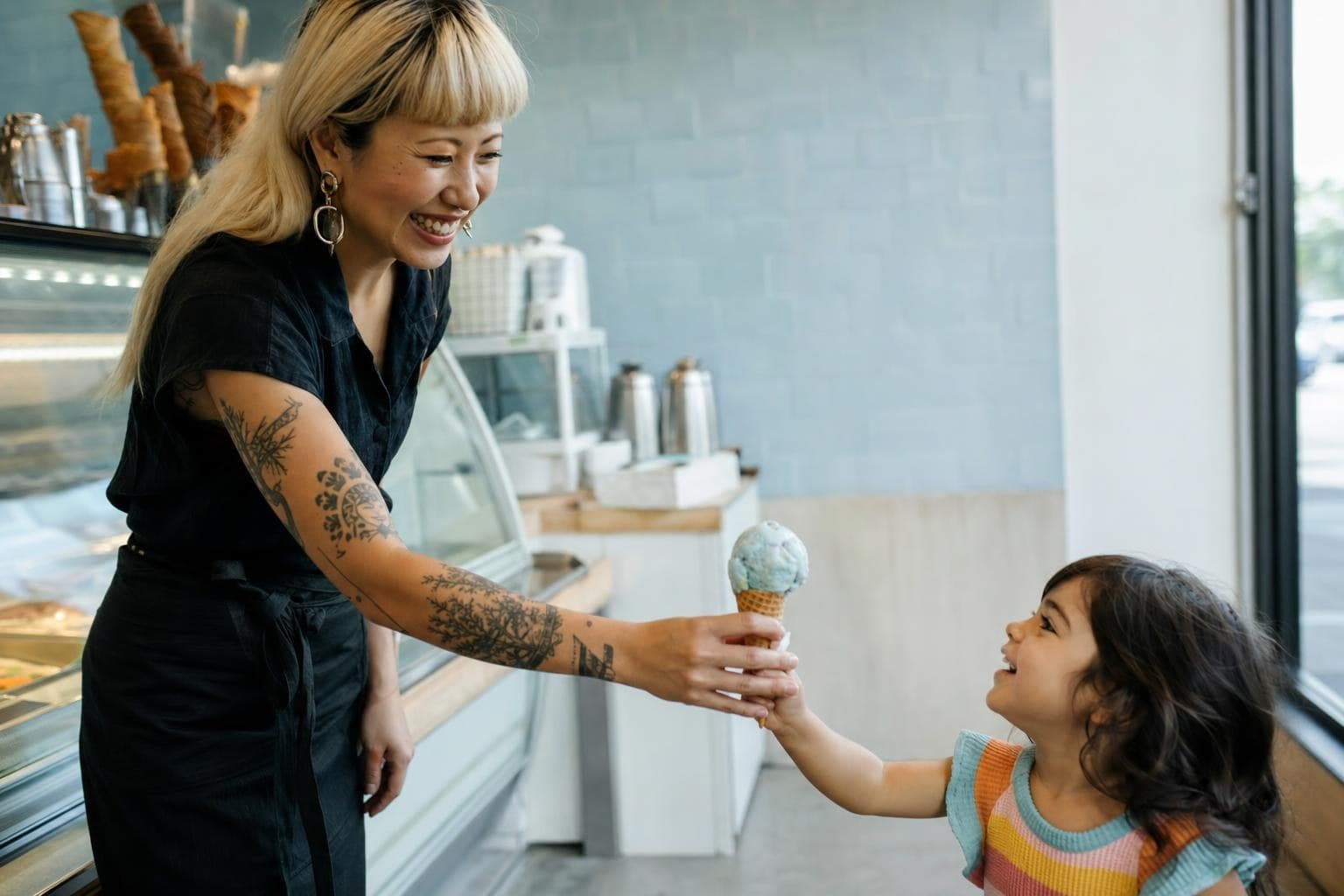 An ice-cream-shop owner with a bold signature look handing a cone to a delighted kid.
